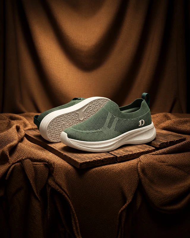 Olive knit sneakers resting on wood with warm draped fabric.